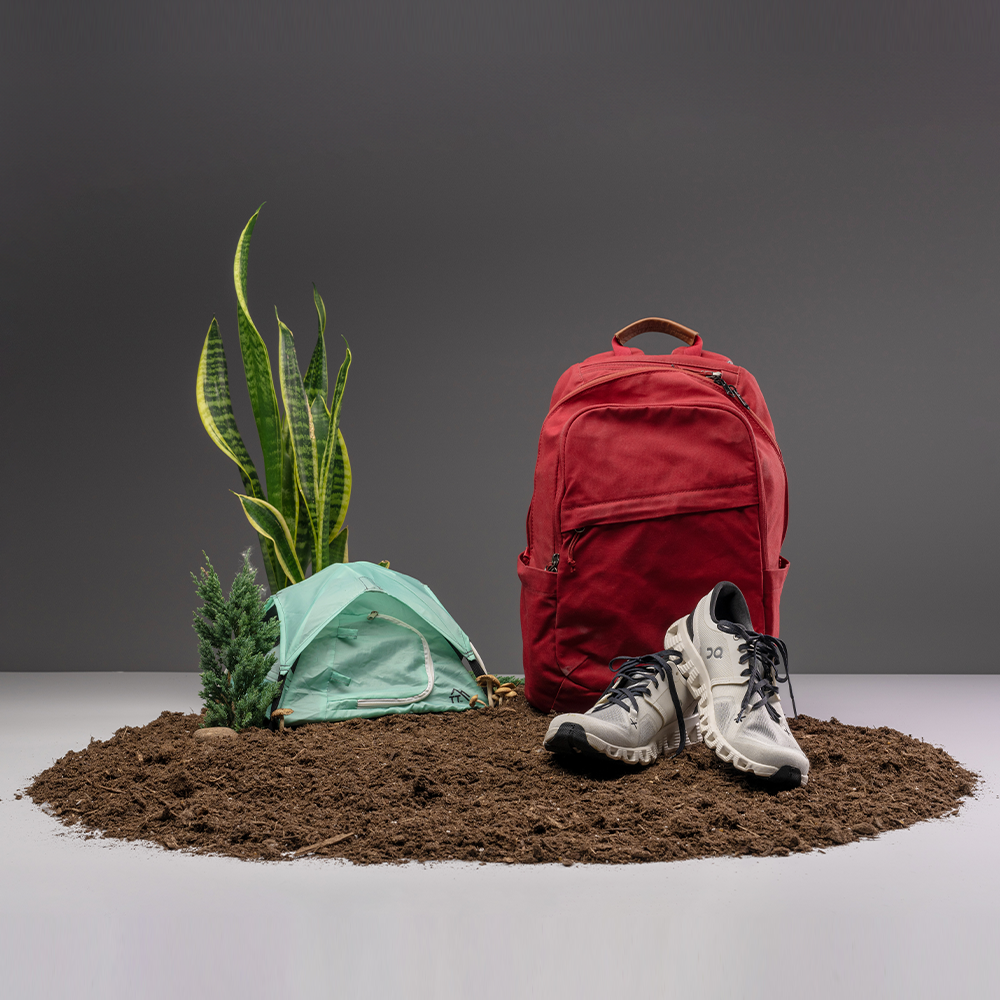 minty teal micro tent in outdoors scene on light gray background. Includes pile of dirt, snake plant, red backpack, and running shoes
